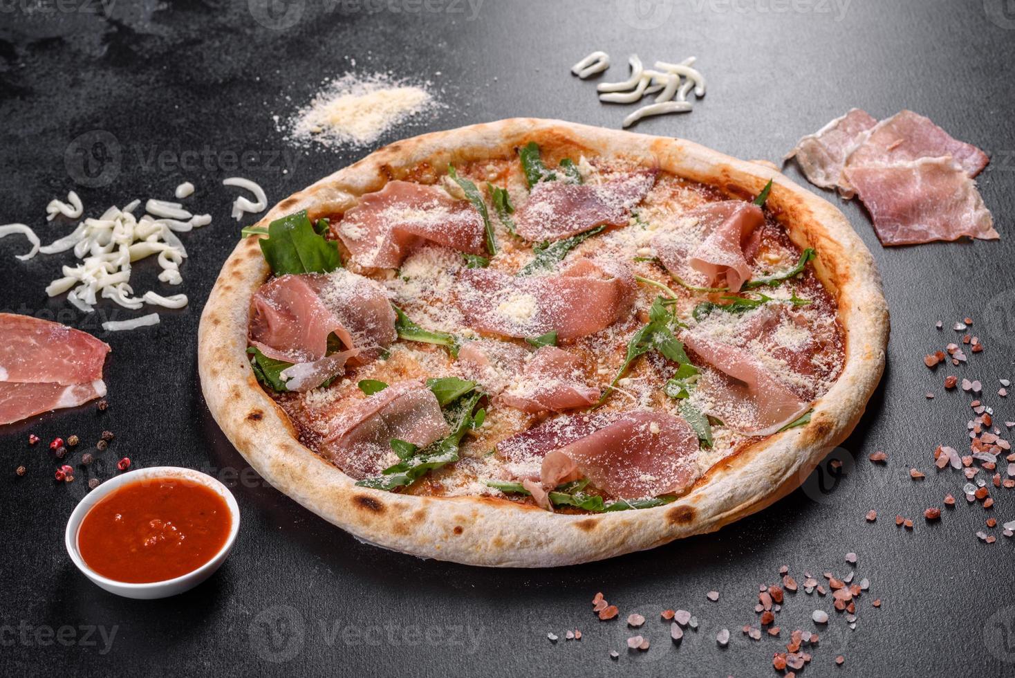 Deliciosa pizza italiana fresca con jamón serrano sobre un fondo de hormigón oscuro foto