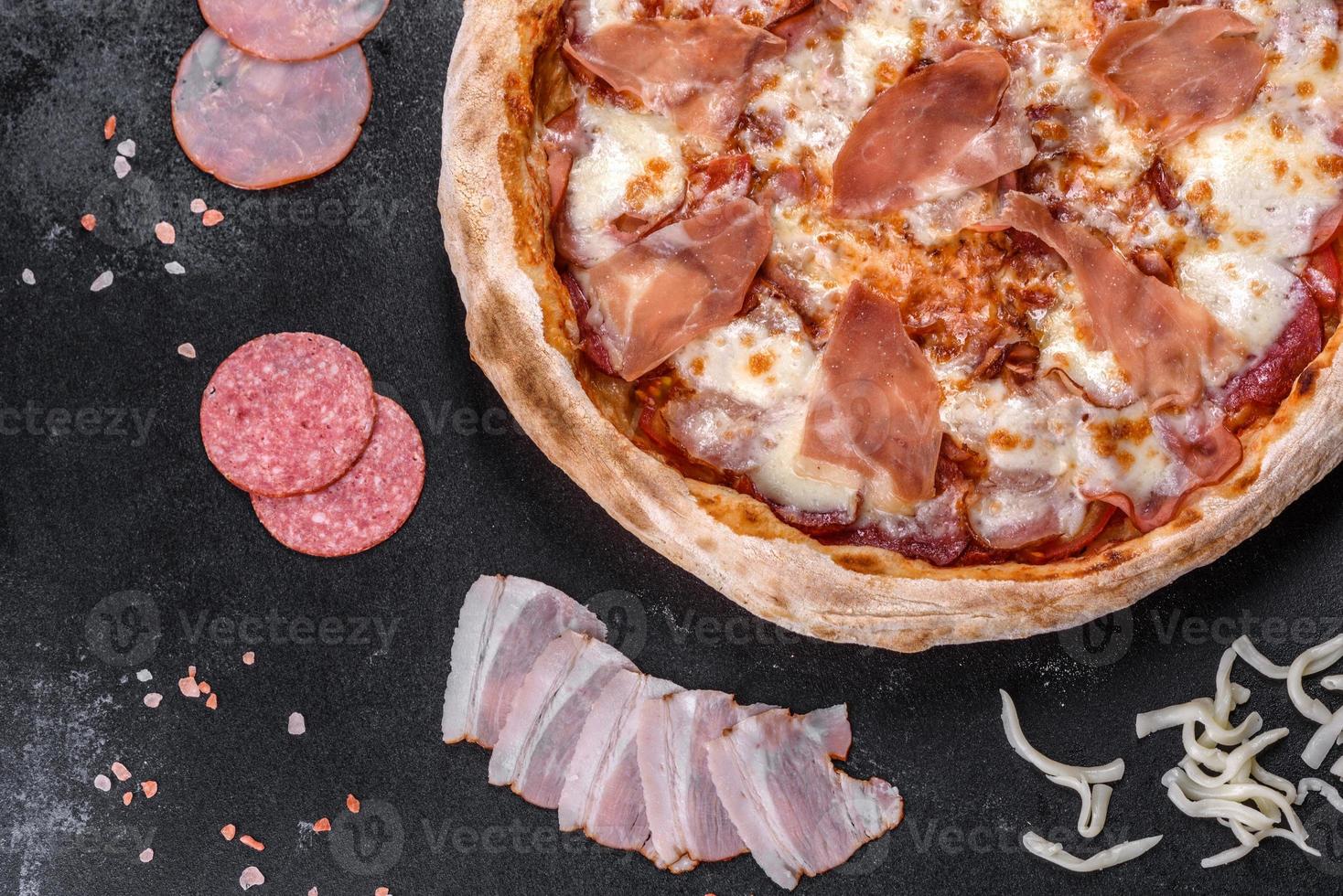 Fresh delicious Italian pizza with a prosciutto on a dark concrete background photo