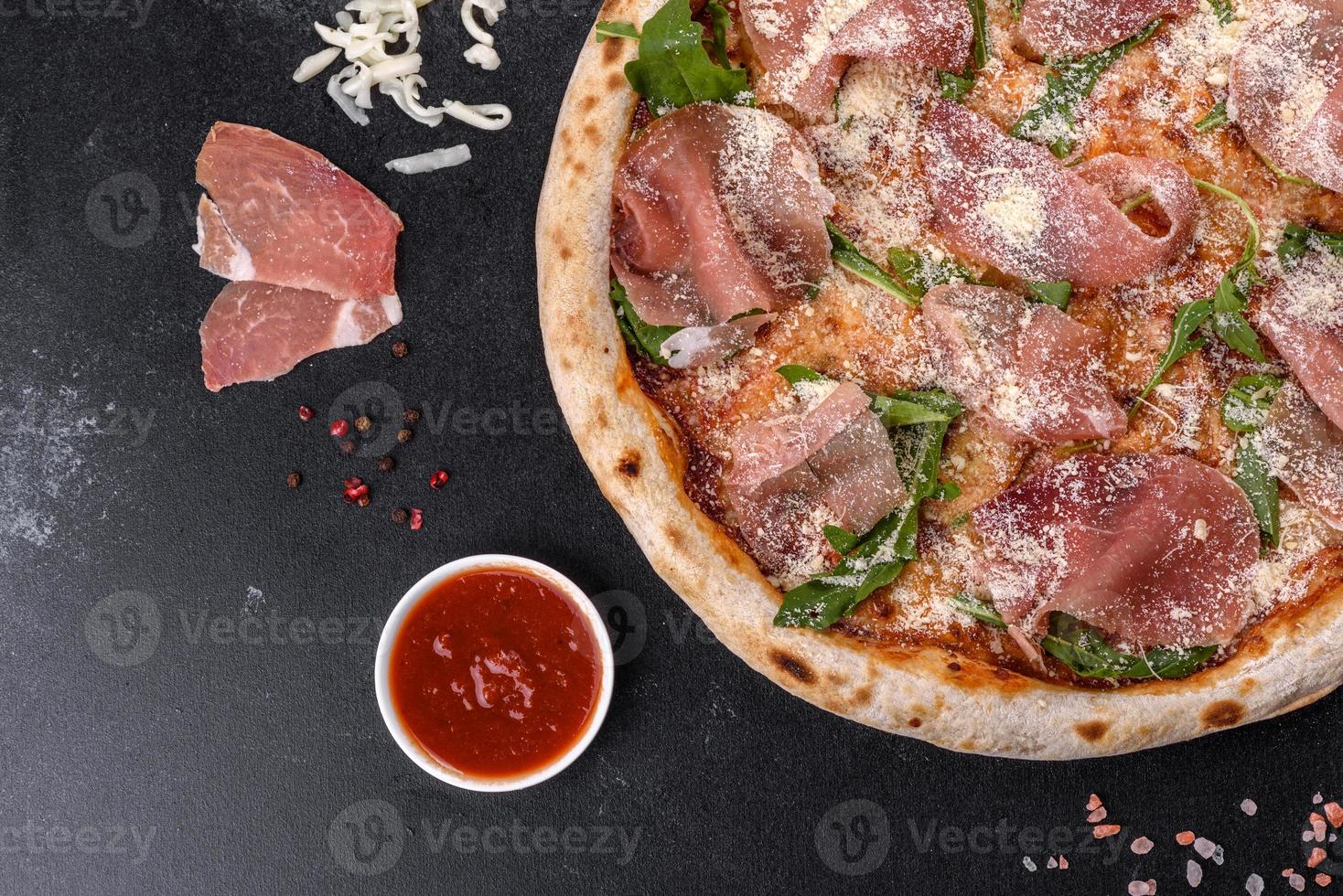 Deliciosa pizza italiana fresca con jamón serrano sobre un fondo de hormigón oscuro foto