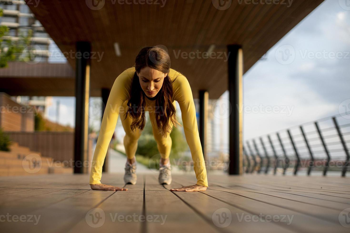 Young woman performing pushups at wooden walkway by the river photo