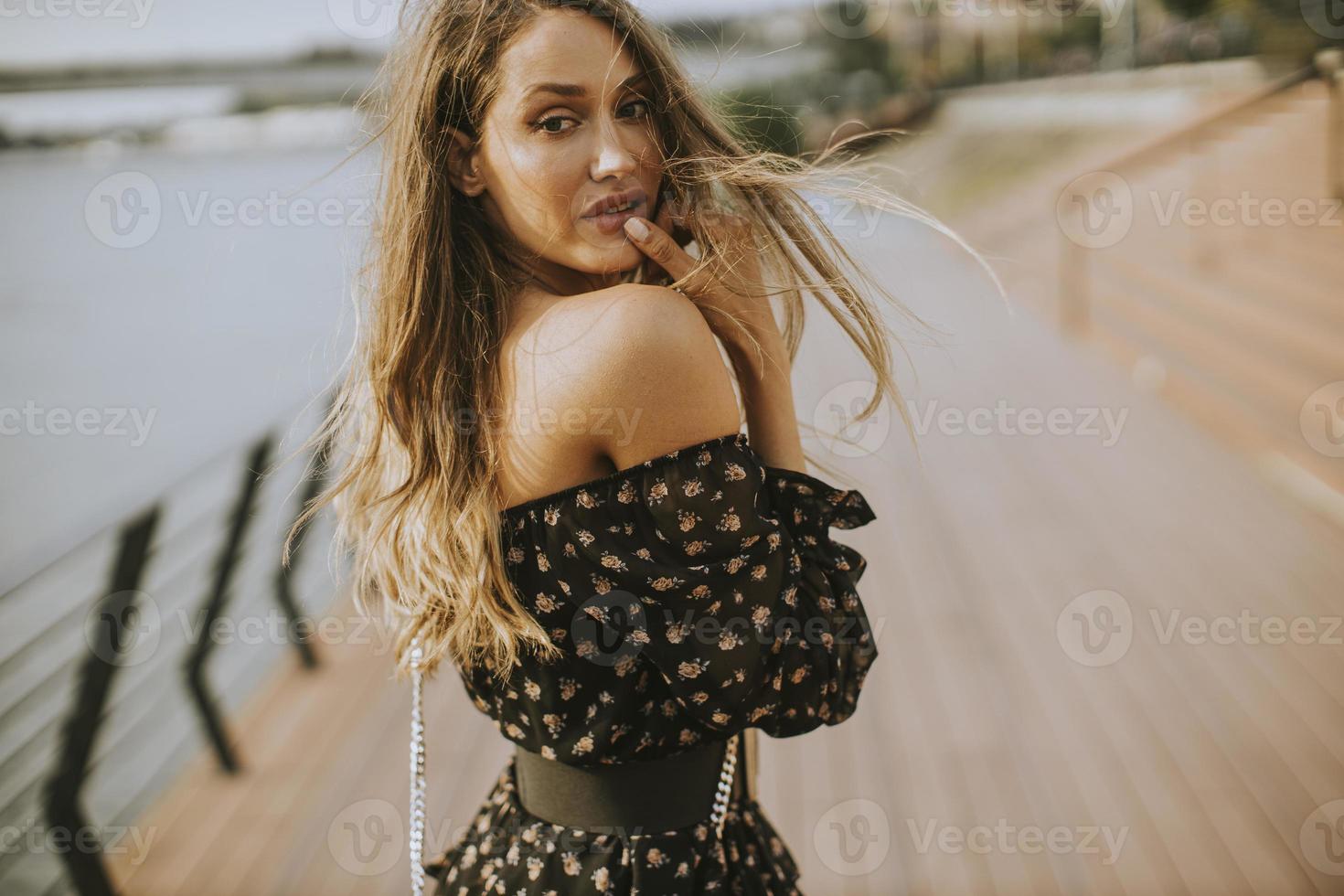 Joven mujer morena de pelo largo caminando por la orilla del río foto