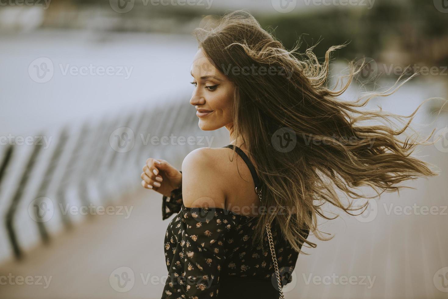 Joven mujer morena de pelo largo caminando por la orilla del río foto