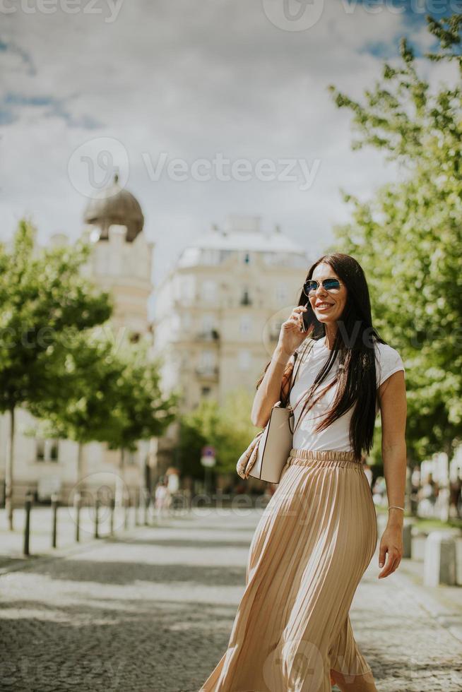 Mujer joven con un teléfono móvil mientras camina por la calle foto