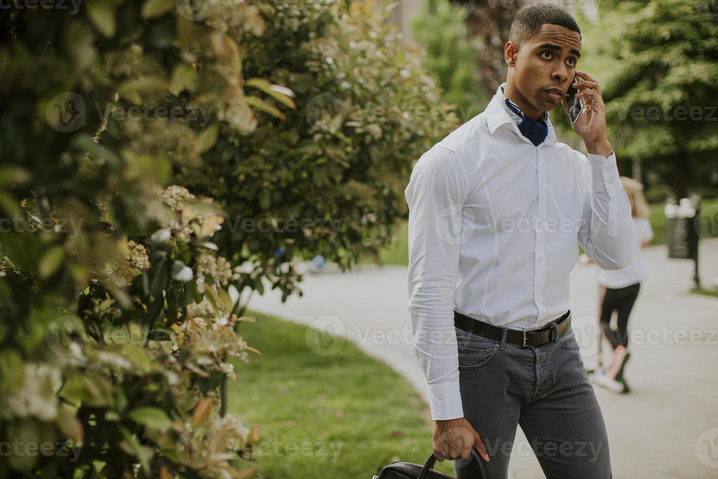 Joven empresario afroamericano mediante un teléfono móvil en una calle foto