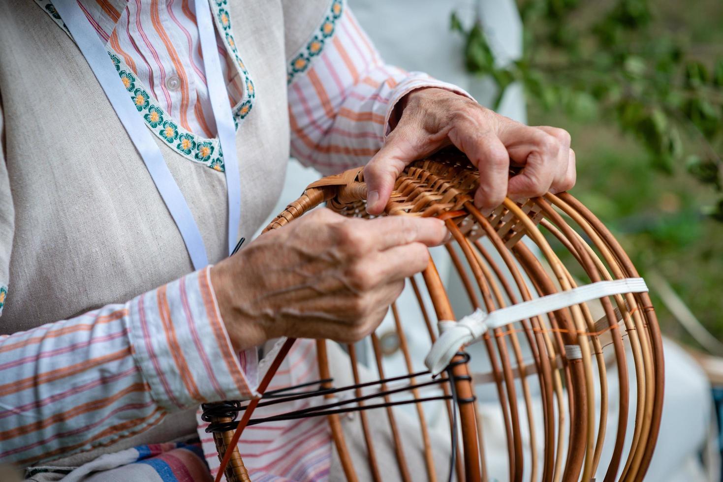 anciana en traje nacional hacer canasta de mimbre local. concepto de artesanía tradicional. letonia - imagen foto