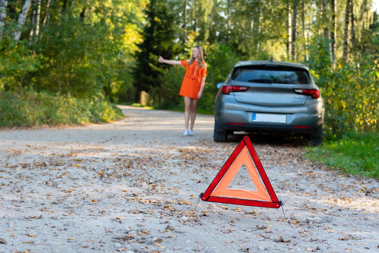 Stressful young woman driver hitchhikes and stops cars, asks for help as have problem with brocken car, uses red triangle sign to warn drivers about stop photo