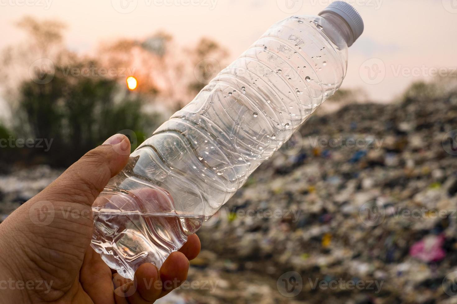 Botella de plástico en la mano del hombre sobre una gran pila de basura y antecedentes de contaminación foto