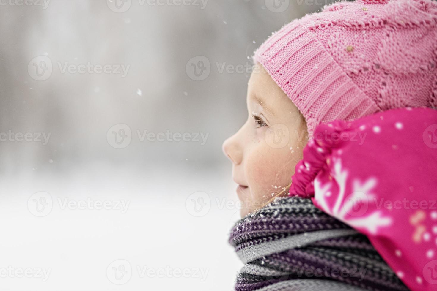 Portrait of a little girl in pink close-up. A child enjoys the snowfall. Christmas holiday photo