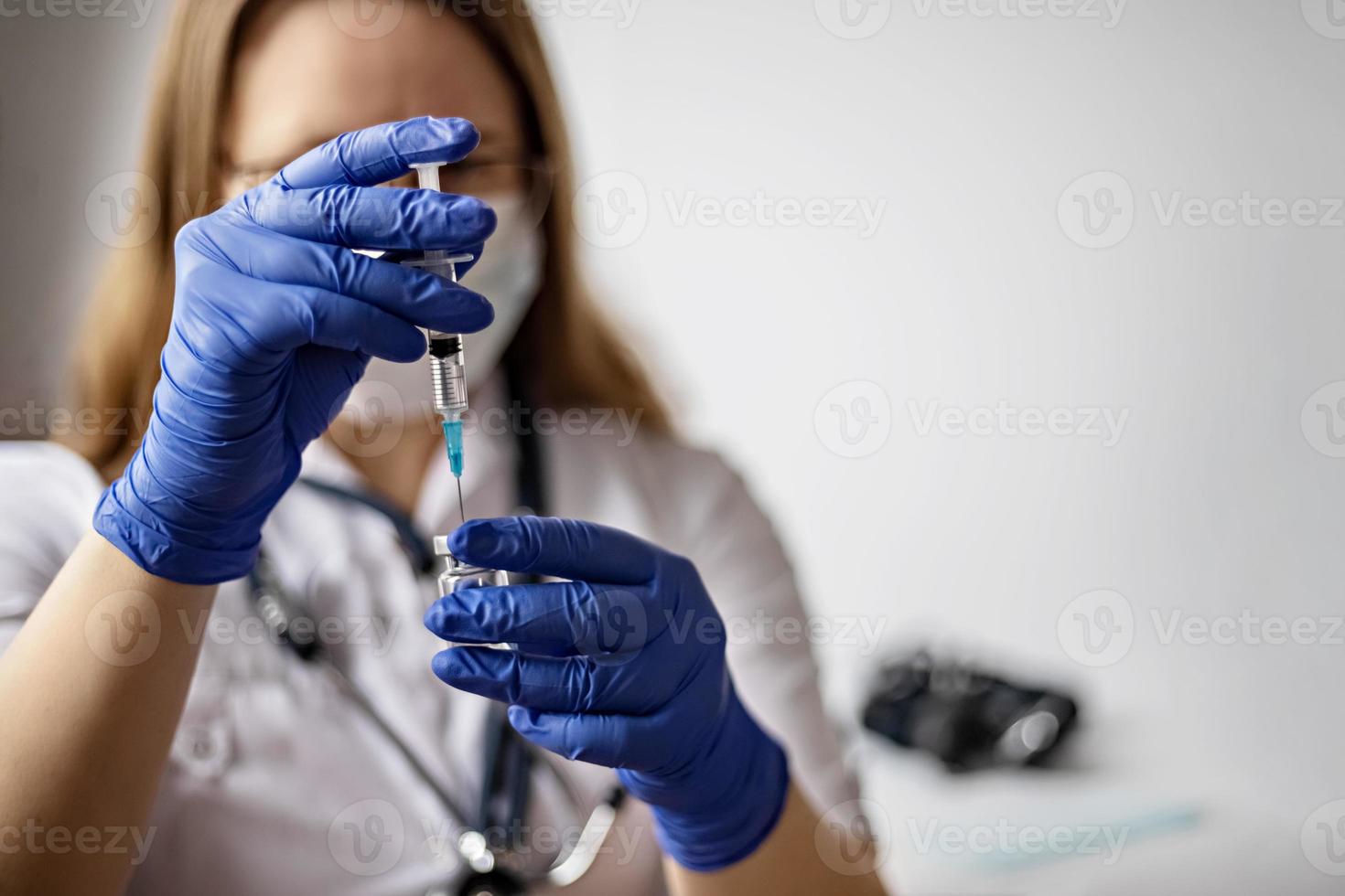 A female doctor wearing a medical mask draws the coronavirus vaccine into a syringe at the clinic.The concept of vaccination, immunization, prevention against Covid-19. photo
