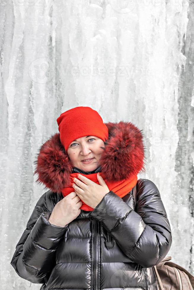 Portrait of a woman in a red hat and scarf, warm jacket against the background of an ice wall. Winter photo