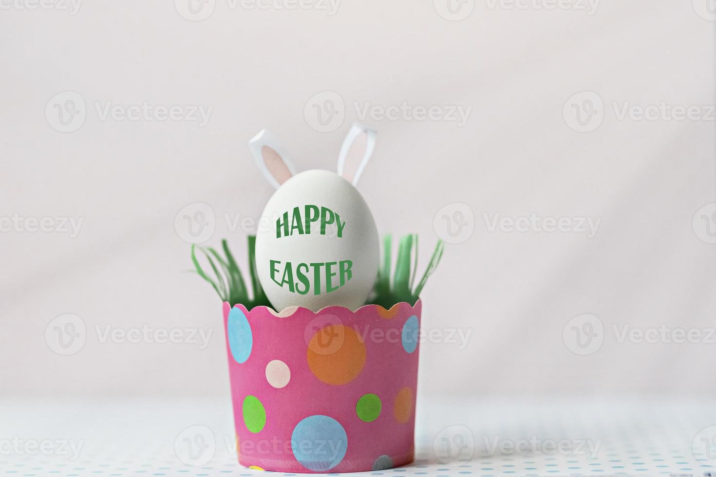 White chicken egg with bunny ears in an eco-friendly pink paper tray, box. Happy Easter holiday concept. English text Happy Easter photo