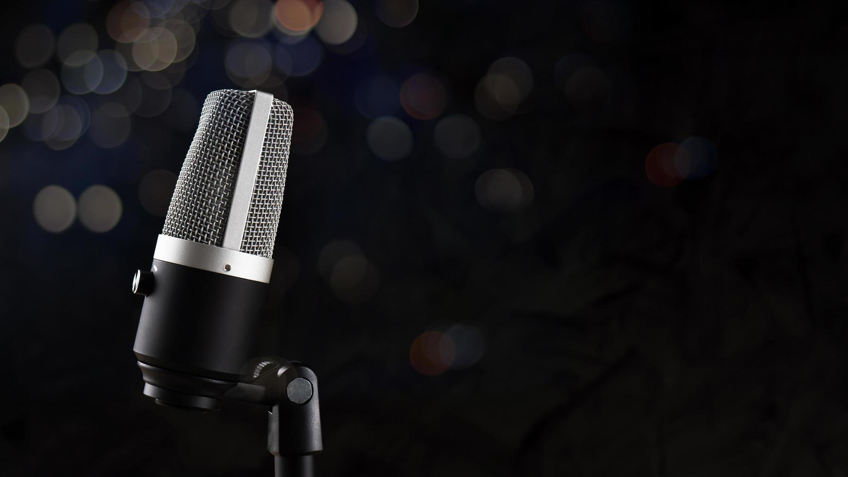 micrófono para grabación de audio o concepto de podcast, micrófono único sobre fondo de sombra oscura y bokeh con espacio de copia foto