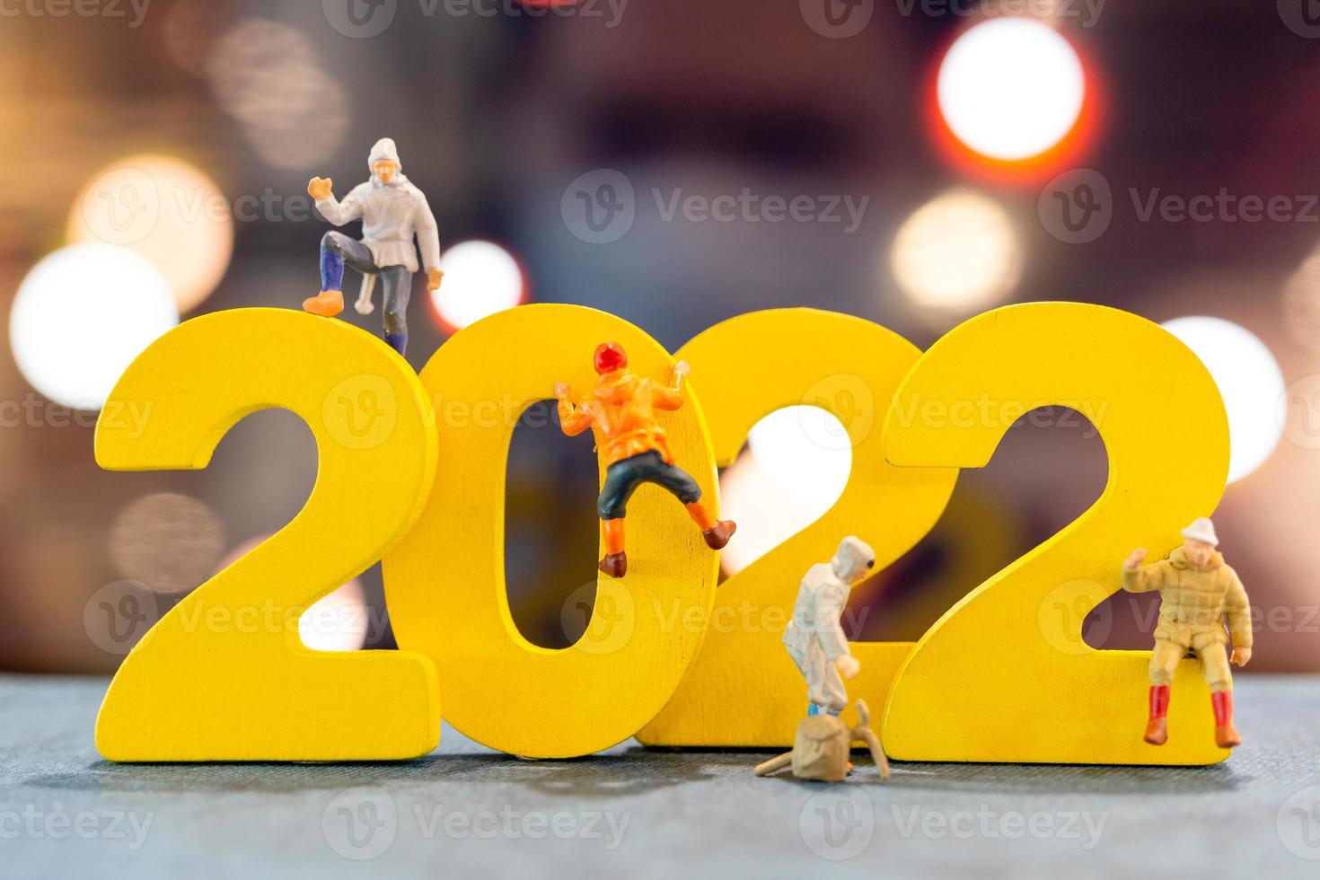 Miniature people climbing up on wooden with number 2022 photo