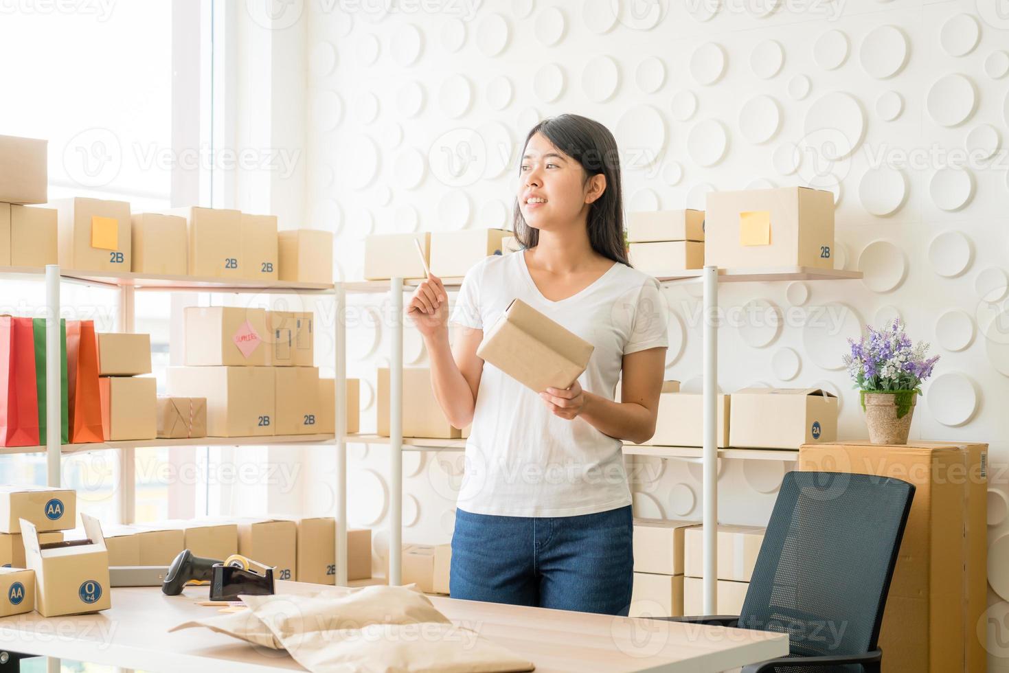 Asian woman business owner working at home with packing box on the workplace - online shopping SME entrepreneur or freelance working concept photo