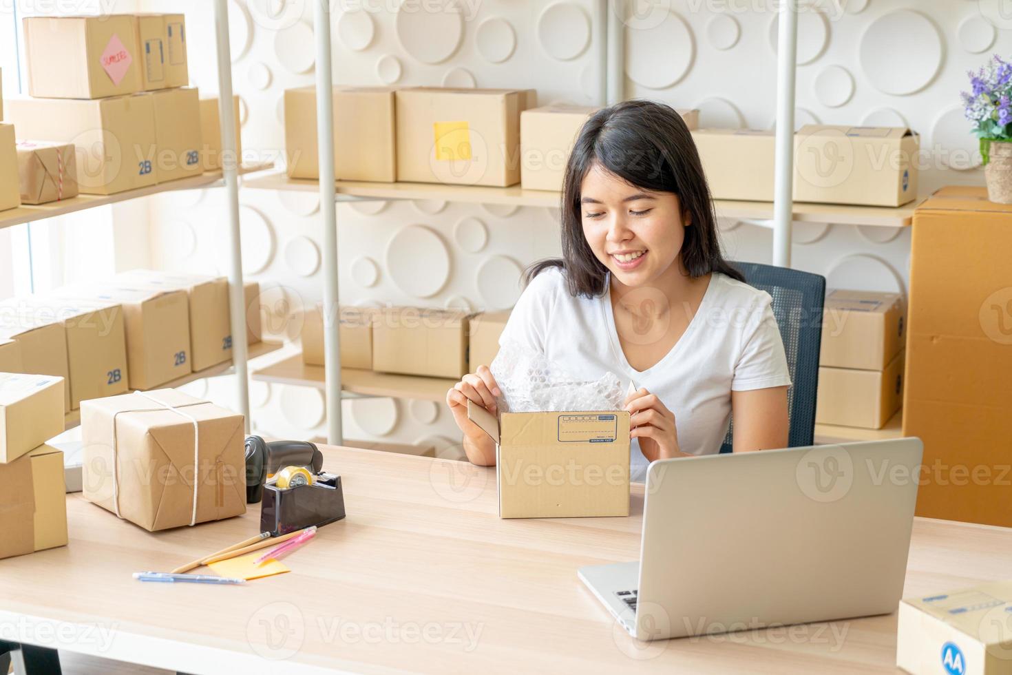 Mujer asiática propietaria de una empresa que trabaja en casa con una caja de embalaje en el lugar de trabajo - emprendedor pyme de compras en línea o concepto de trabajo independiente foto