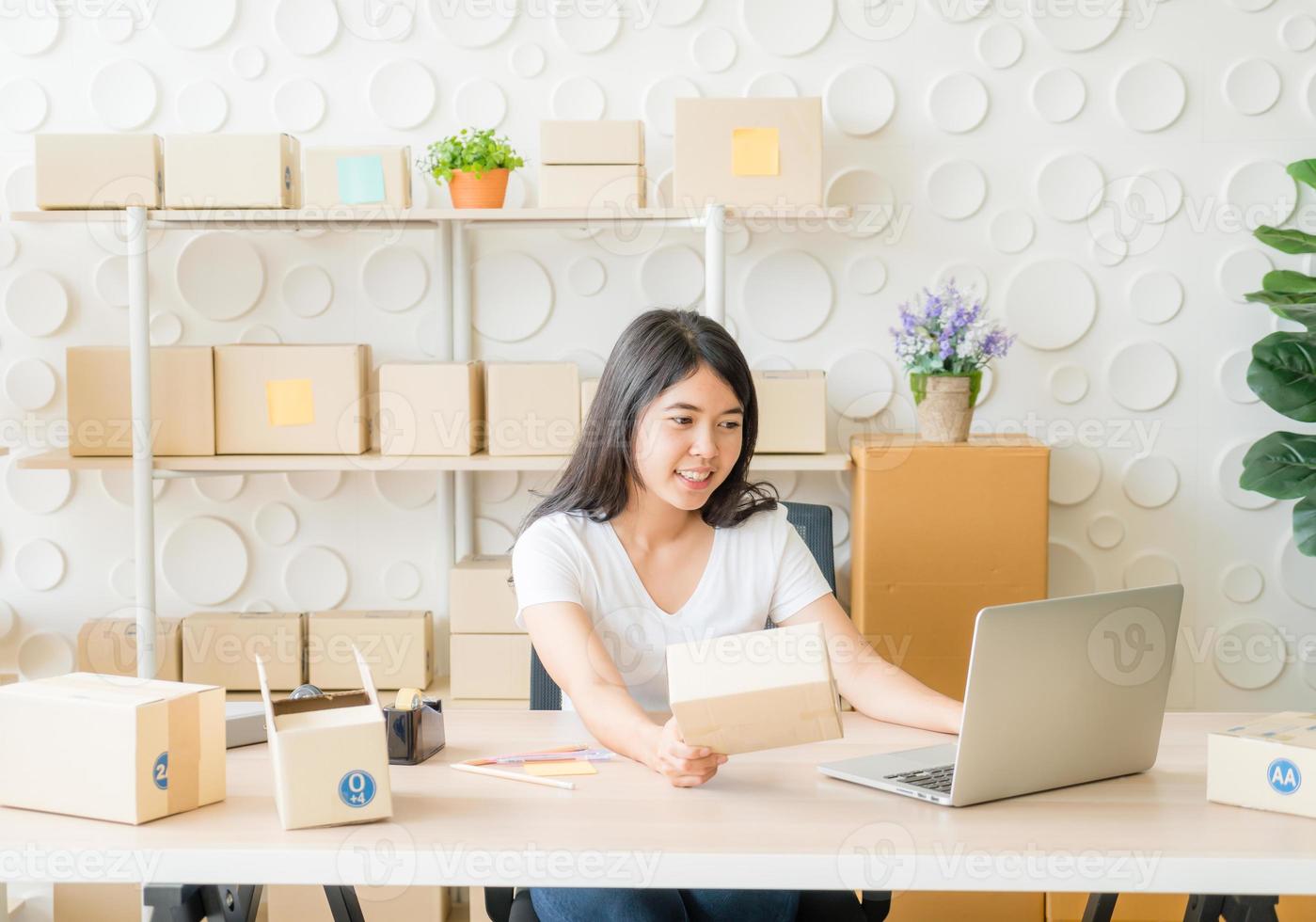 Mujer asiática divirtiéndose mientras usa internet en la computadora portátil y el teléfono en la oficina - vender en línea o concepto de compras en línea foto