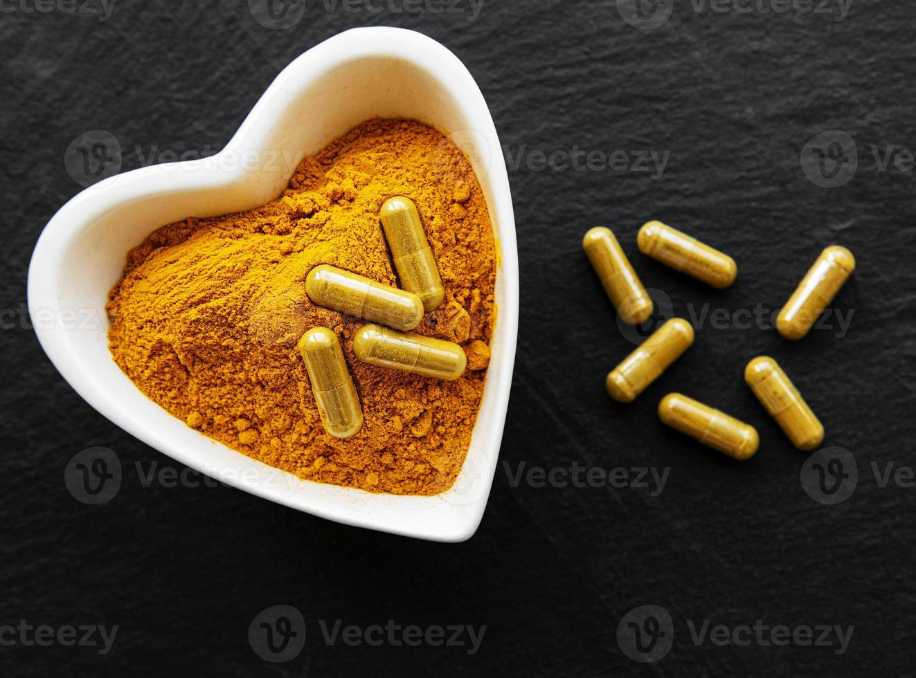 Turmeric powder and turmeric pills on a black concrete background photo