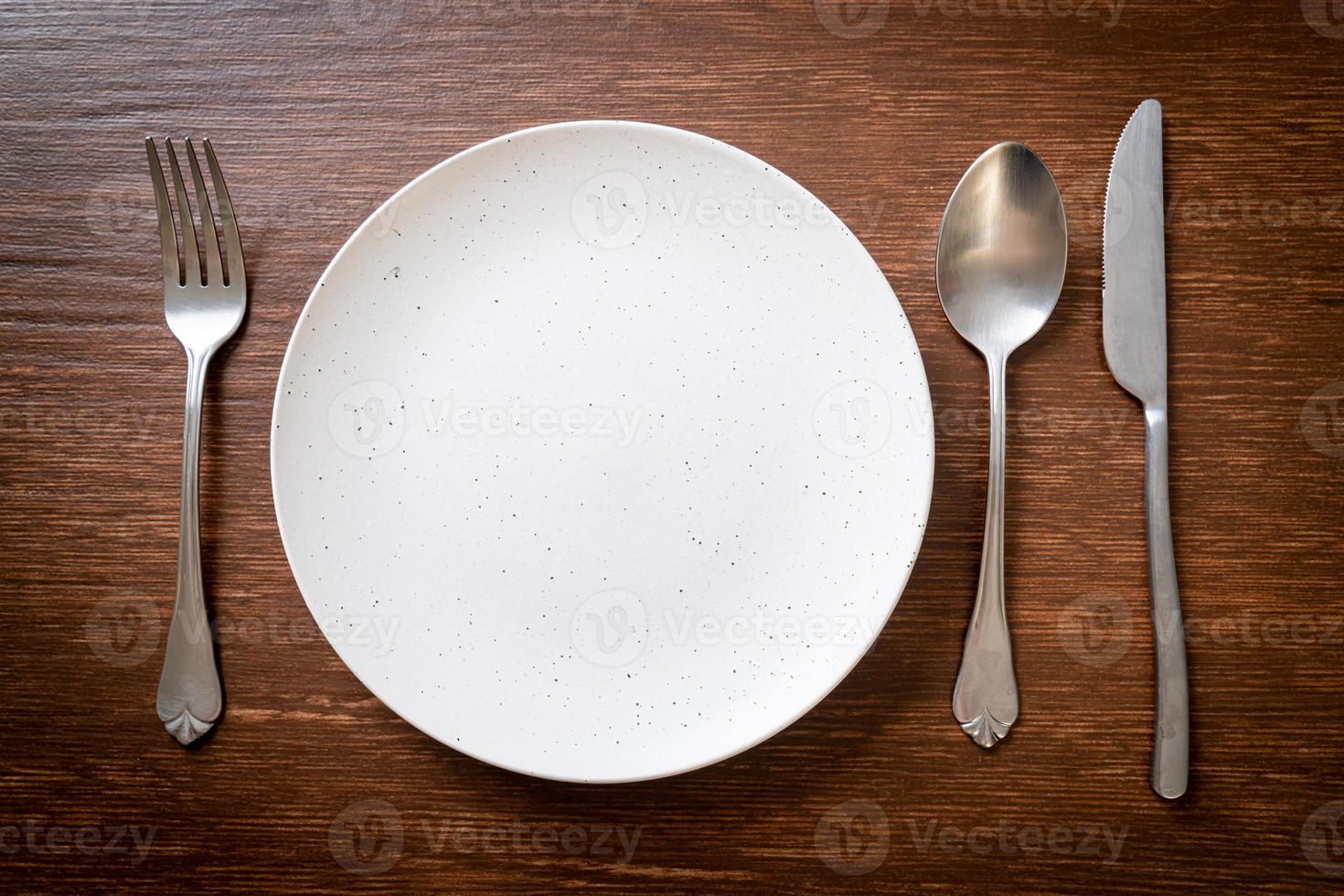 Empty plate or dish with knife, fork, and spoon on wood tile background photo