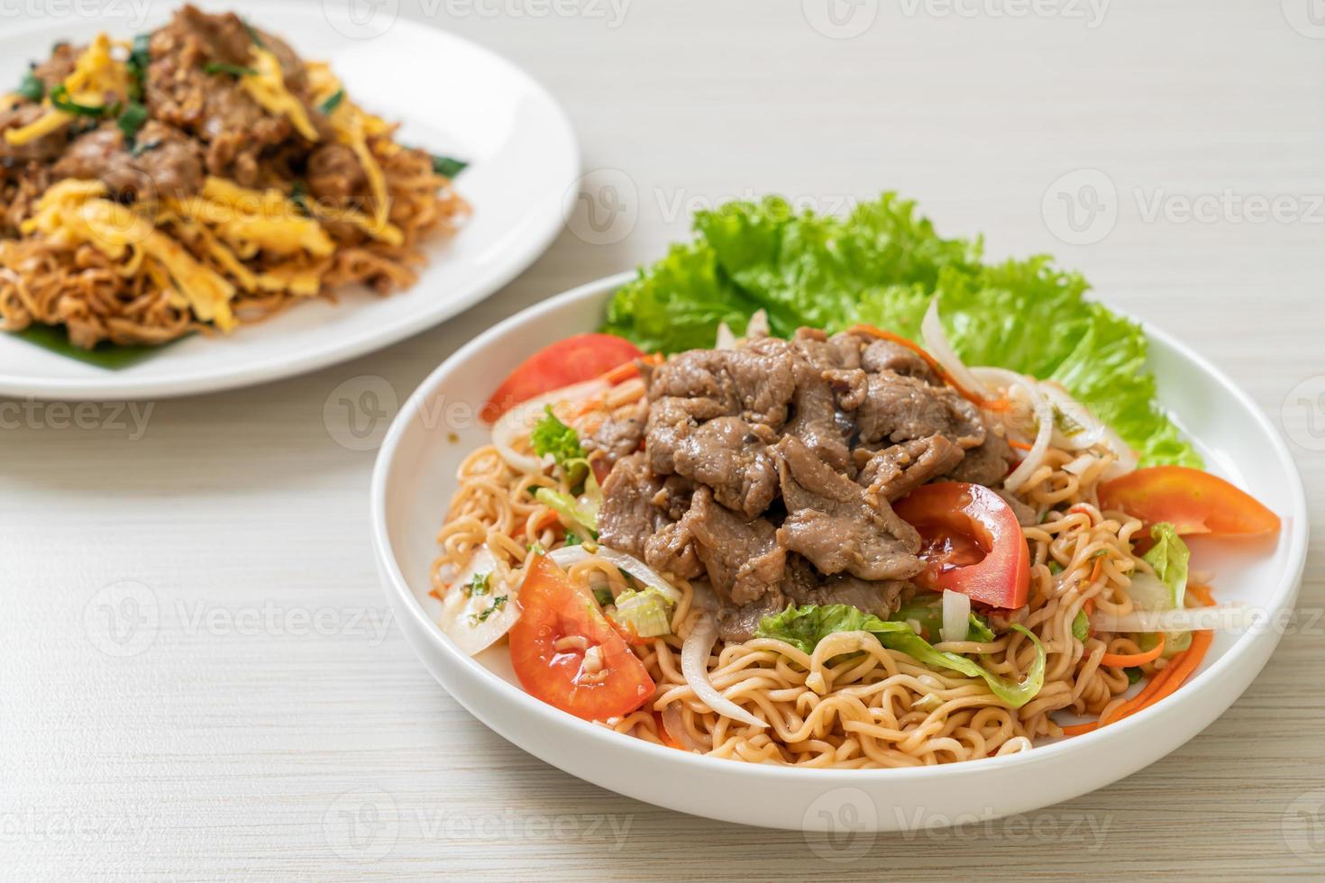 Ensalada picante de fideos instantáneos con carne de cerdo en un plato blanco - estilo de comida asiática foto
