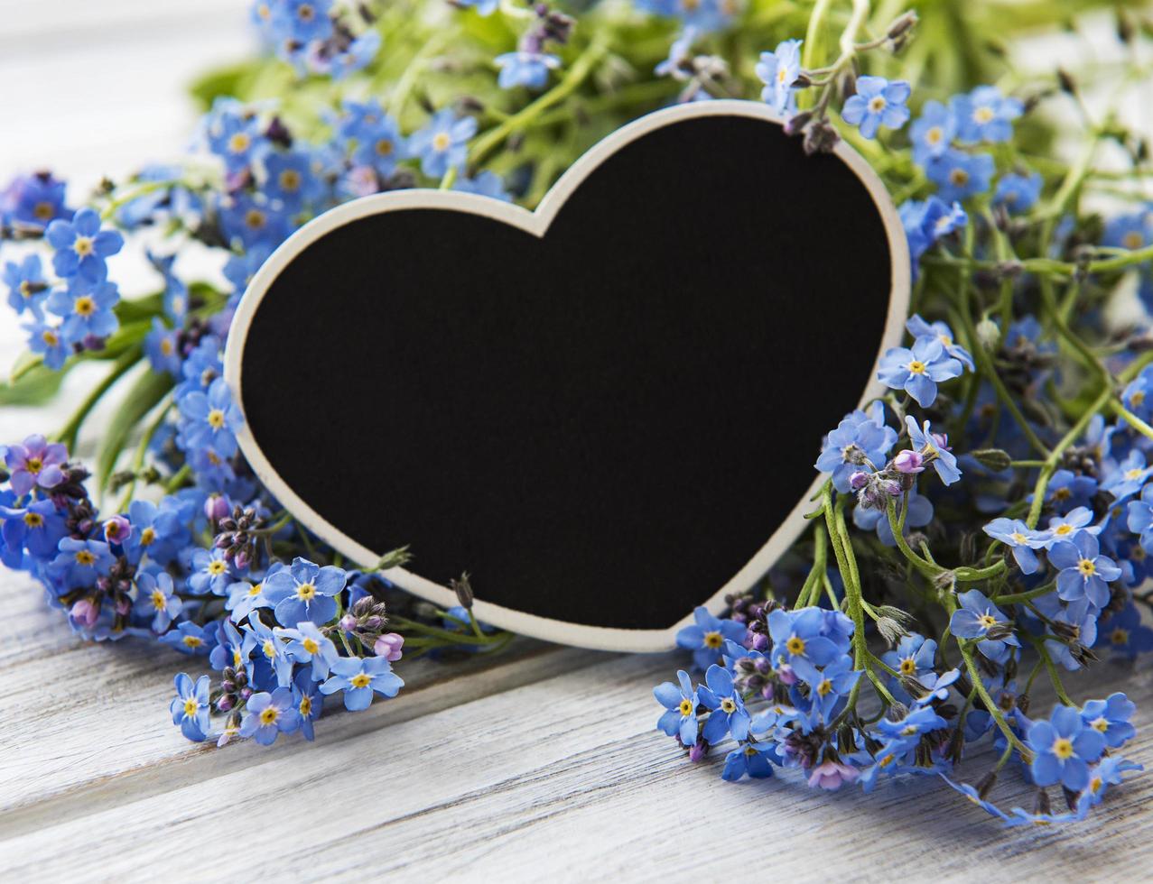 Nomeolvides flores y tablero en forma de corazón negro sobre fondo blanco de madera foto