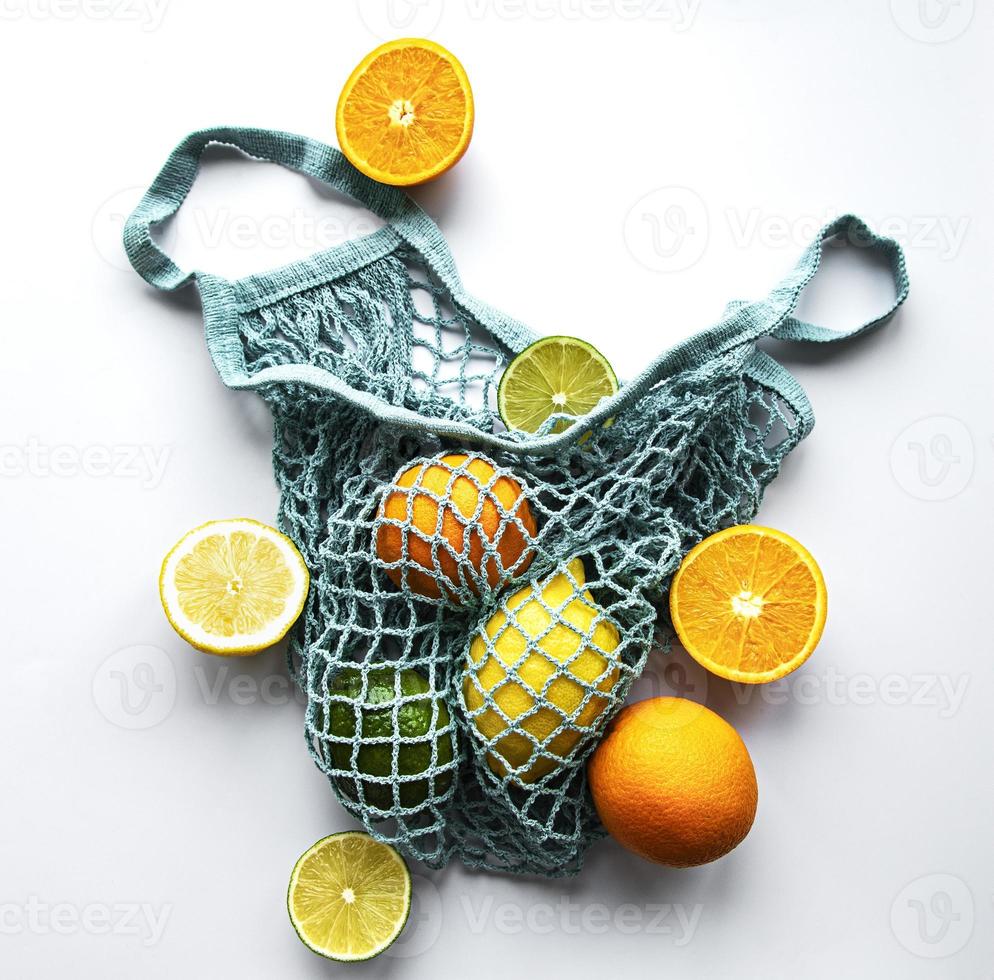 Ripe whole citrus fruits in string bag on white background photo