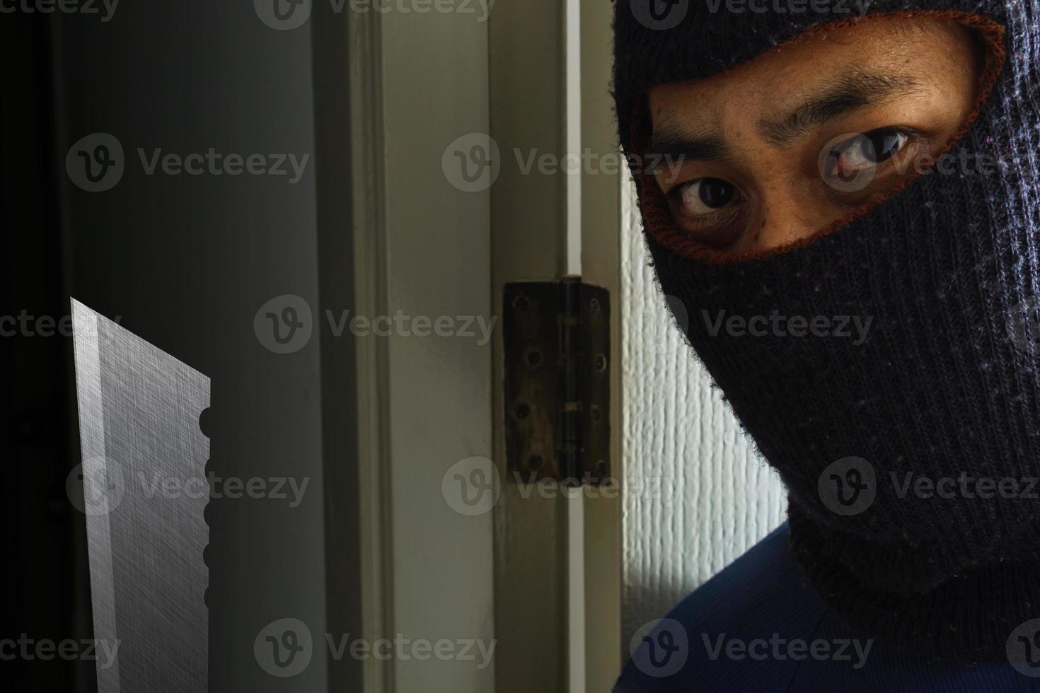 Masked robber with knife hiding behind the door photo