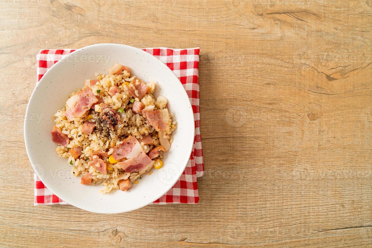 Arroz frito con tocino, jamón y pimientos negros en la placa blanca. foto