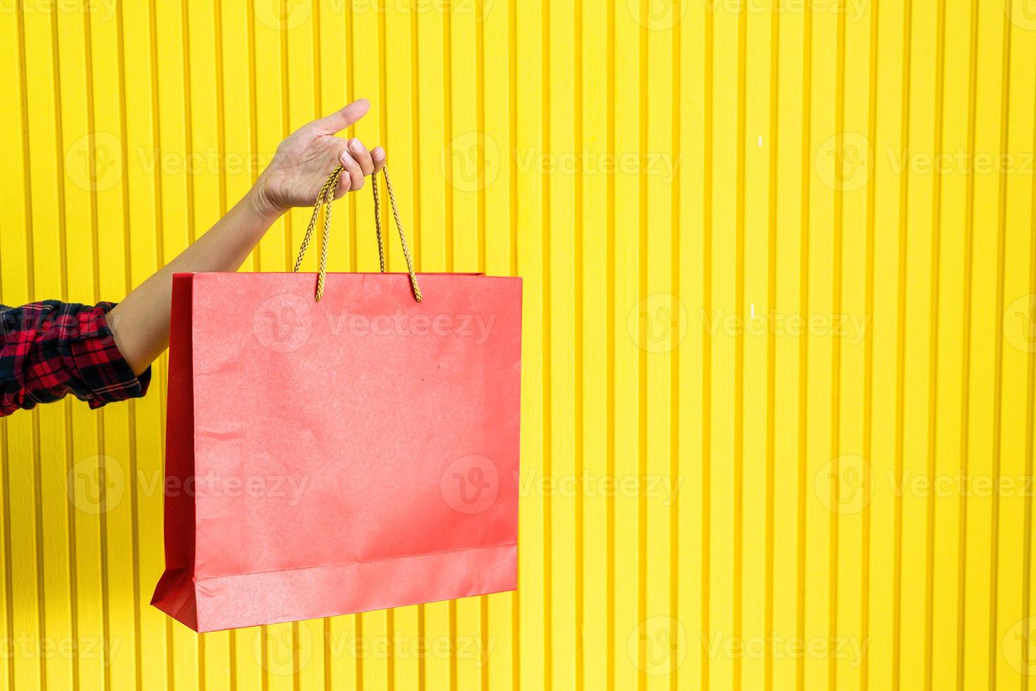 Red shopping bag on hand with yellow wall for copy space photo