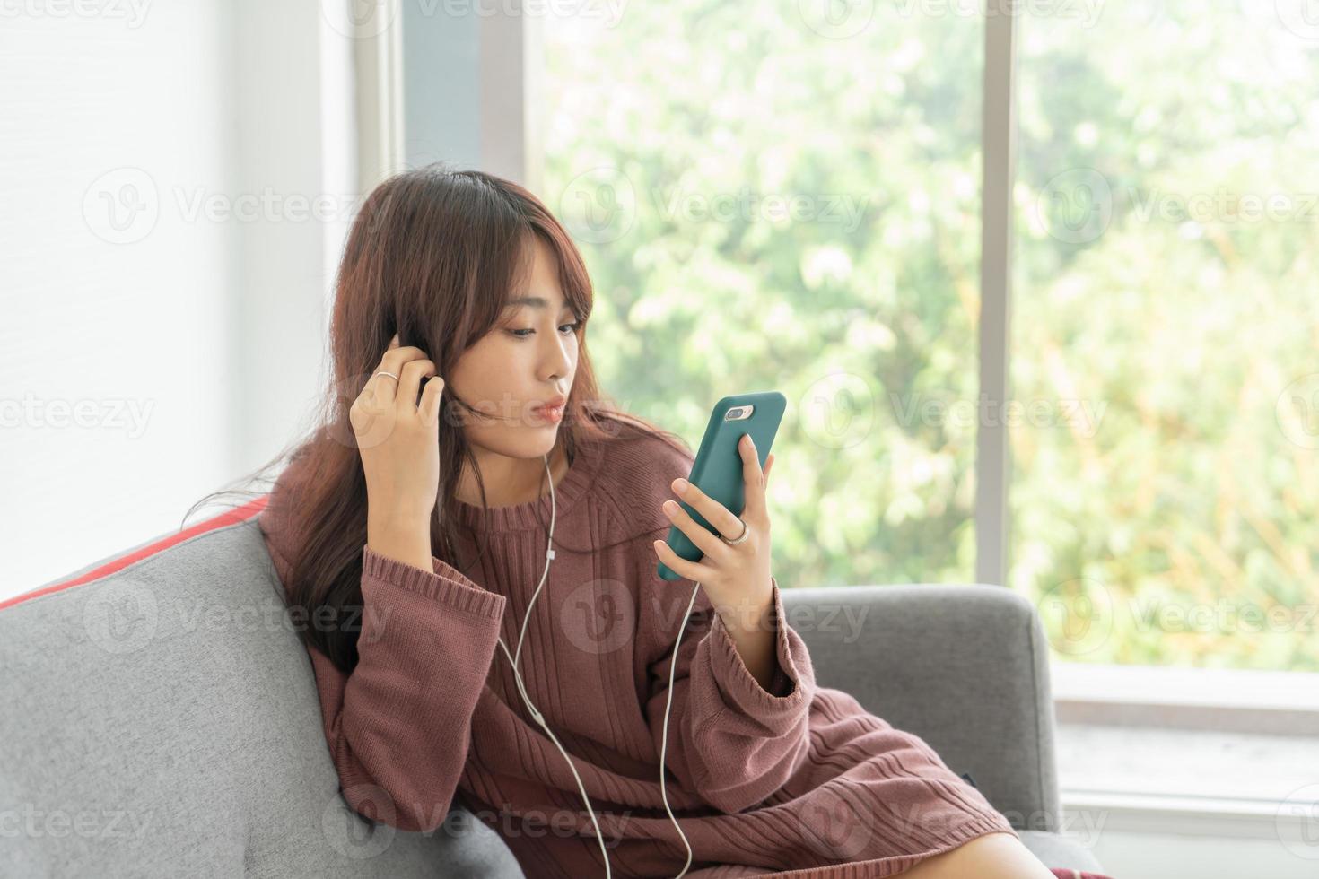 Beautiful Asian woman using smartphone on grey sofa in living room photo