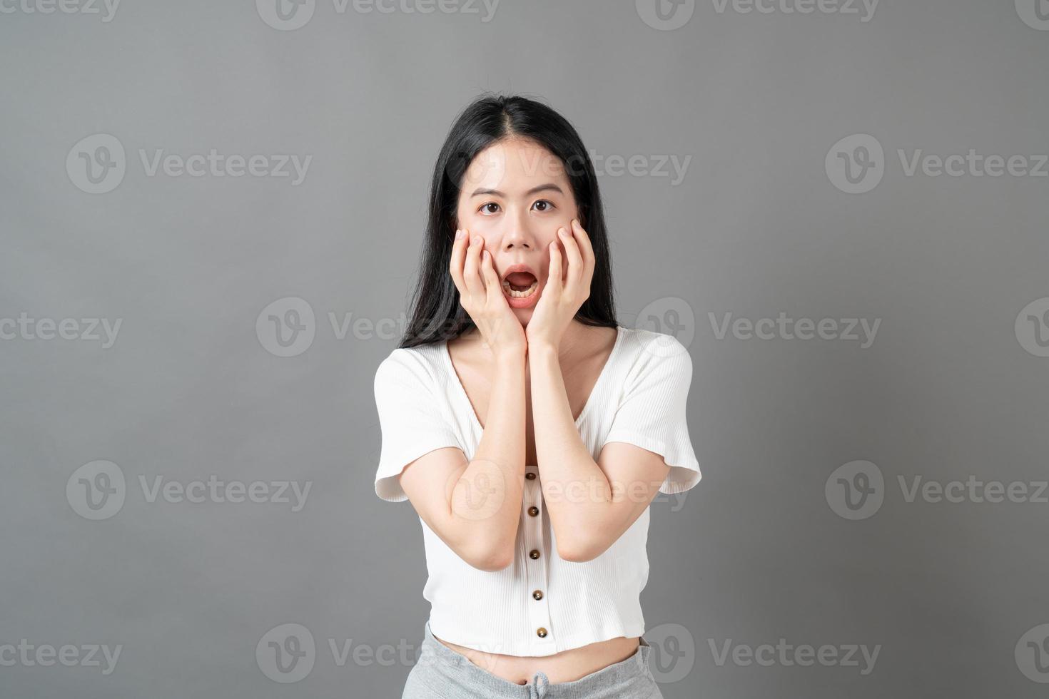 Joven mujer asiática con cara seria y tensa en camisa blanca sobre fondo gris foto