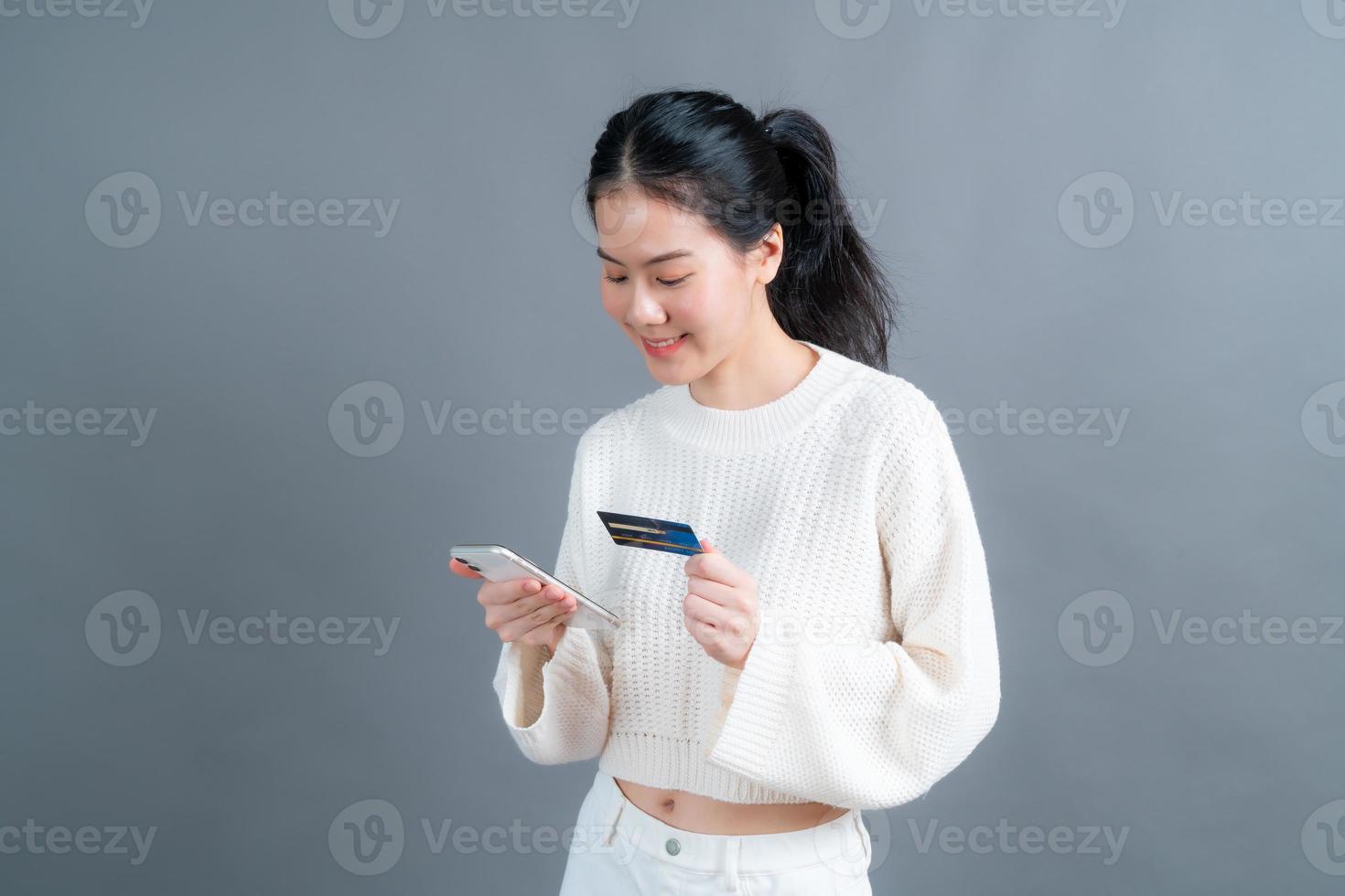 Young Asian girl showing plastic credit card while holding mobile phone photo