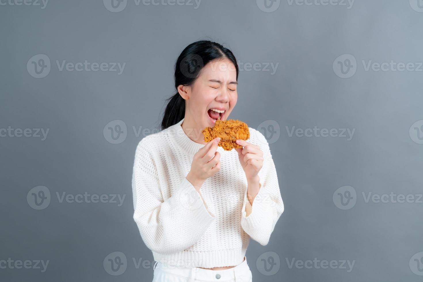 joven asiática vistiendo un suéter disfruta comiendo pollo frito foto