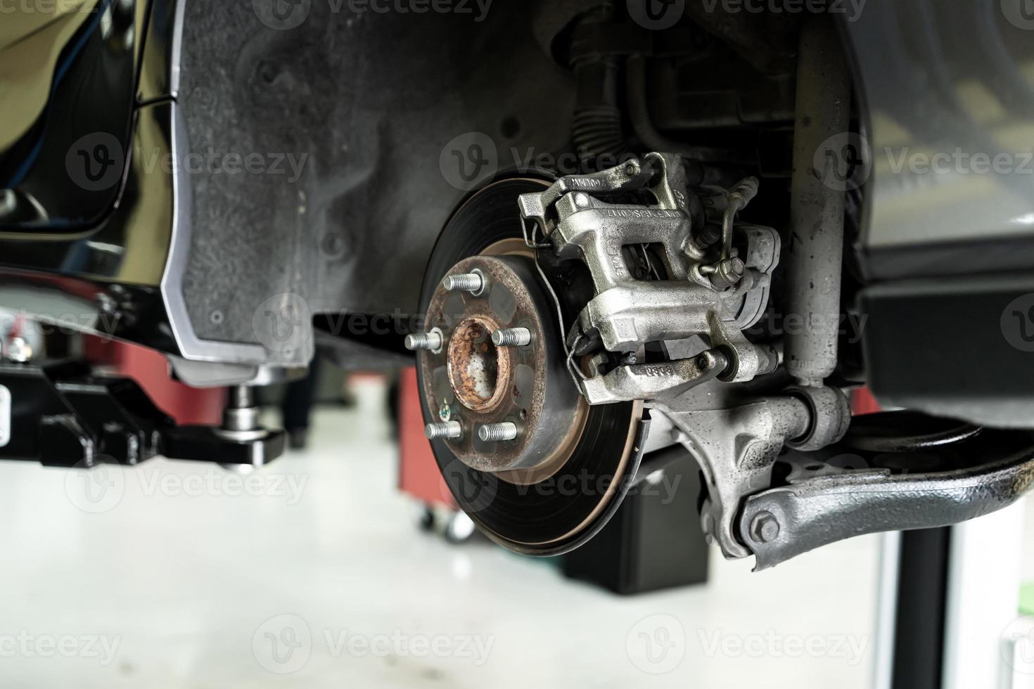 Disc car close up - mechanic unscrewing automobile parts while working under a lifted auto photo
