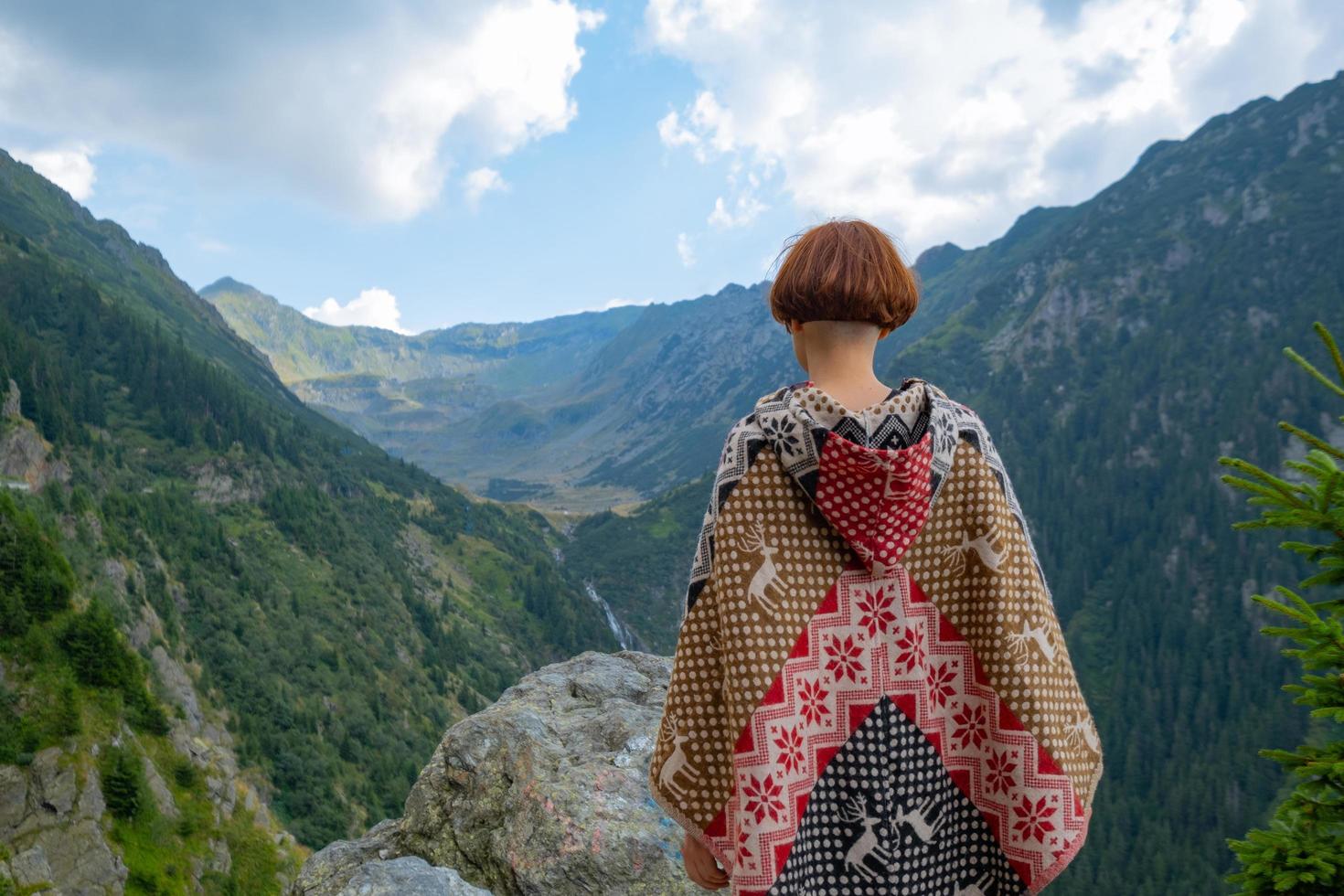 Woman traveler in poncho posing in the mountains photo