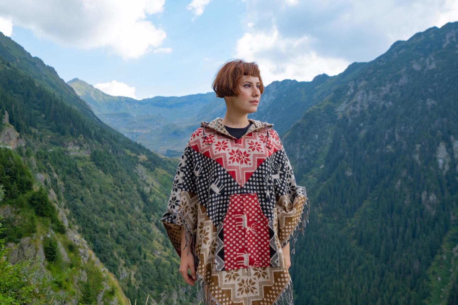 Woman traveler in poncho posing in the mountains photo