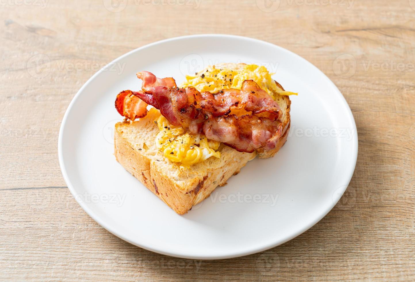 Tostadas de pan con huevos revueltos y tocino en la placa blanca. foto