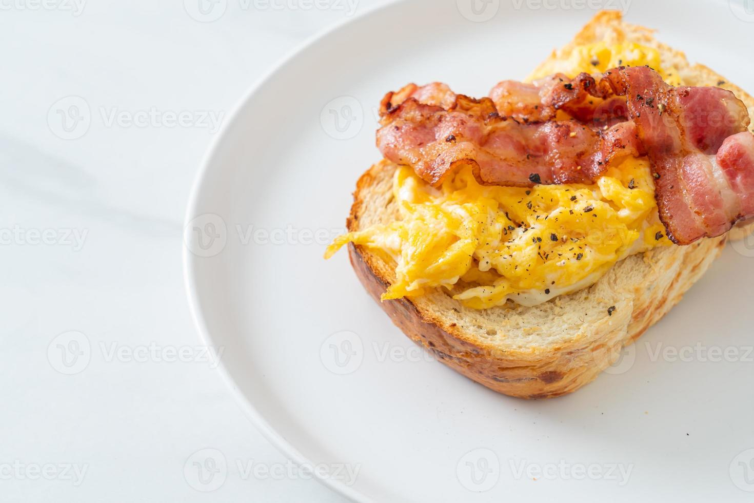 Tostadas de pan con huevos revueltos y tocino en la placa blanca. foto