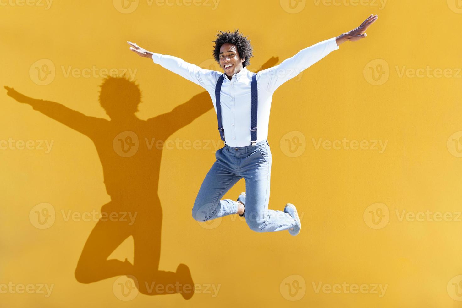 Hombre negro con cabello afro saltando sobre un fondo urbano amarillo foto