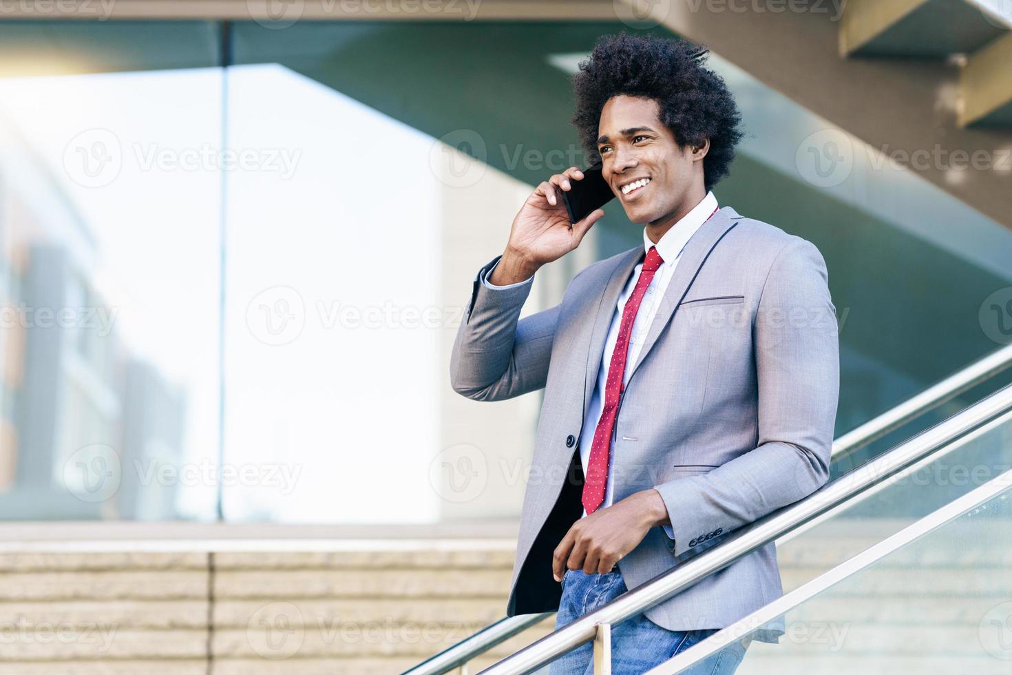 empresario negro usando un teléfono inteligente cerca de un edificio de oficinas foto