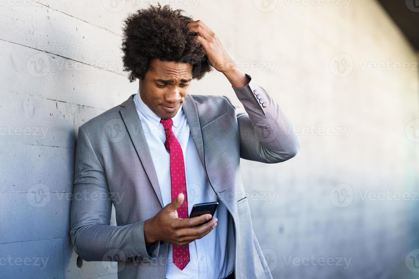 Hombre de negocios negro preocupado que usa su teléfono inteligente al aire libre. foto