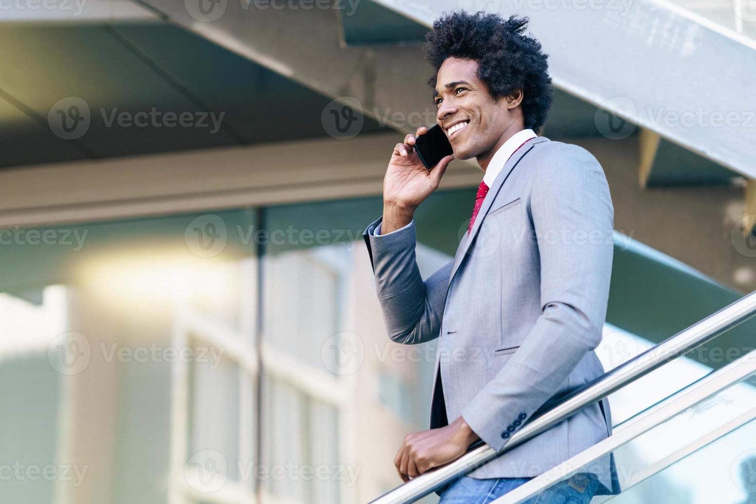 empresario negro usando un teléfono inteligente cerca de un edificio de oficinas foto