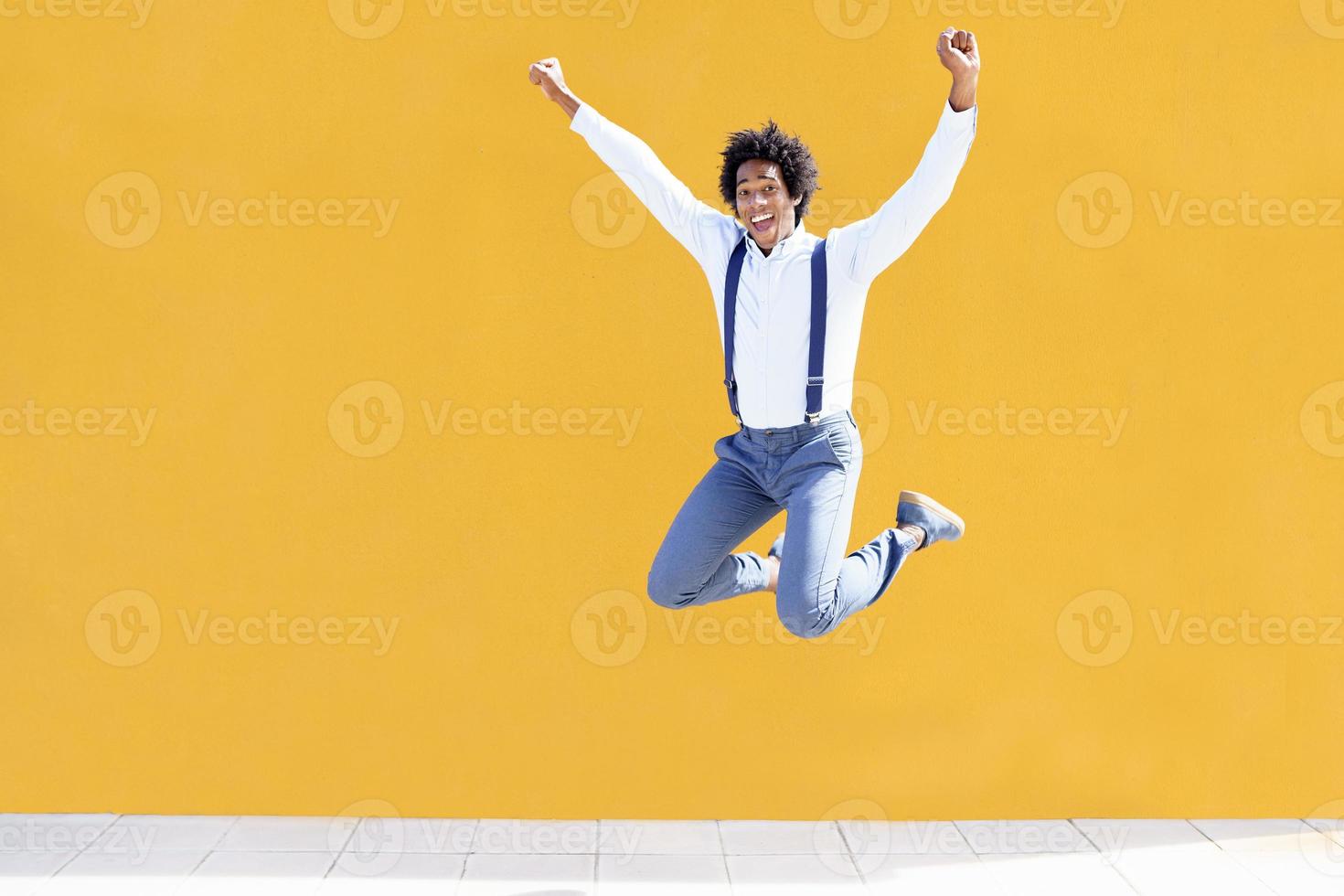 Hombre negro con cabello afro saltando sobre un fondo urbano amarillo foto