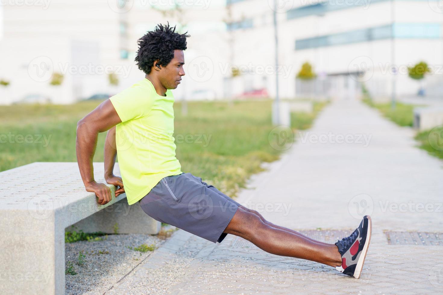 Hombre negro haciendo ejercicio de inmersión de tríceps en un banco de la calle de la ciudad. foto