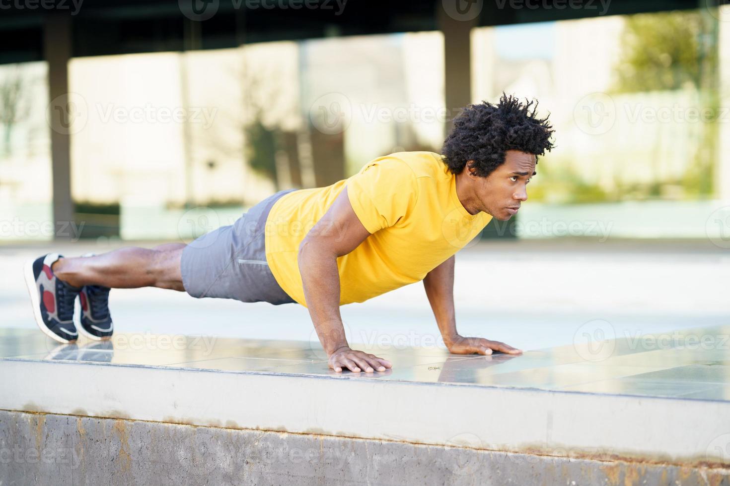 Black man doing triceps dip exercise on city street bench. photo