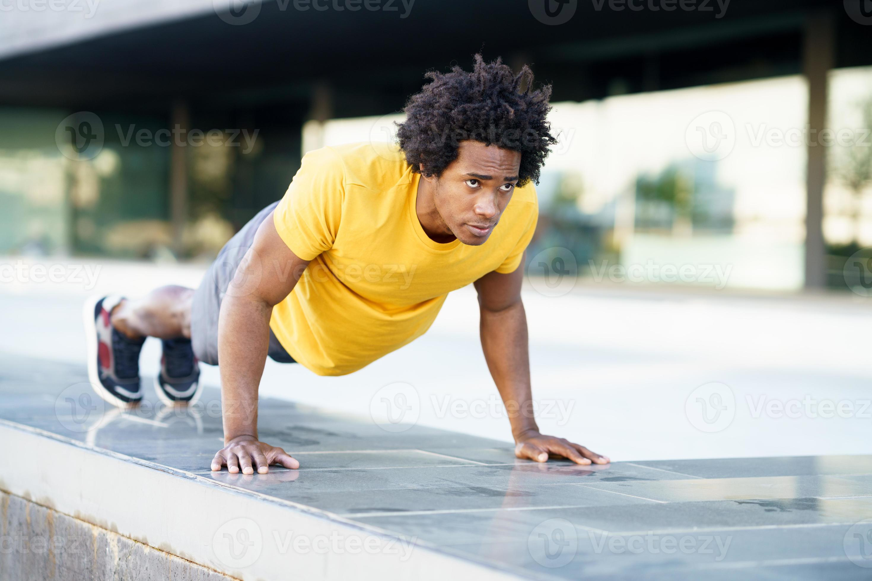 Black man doing triceps dip exercise on city street bench. photo