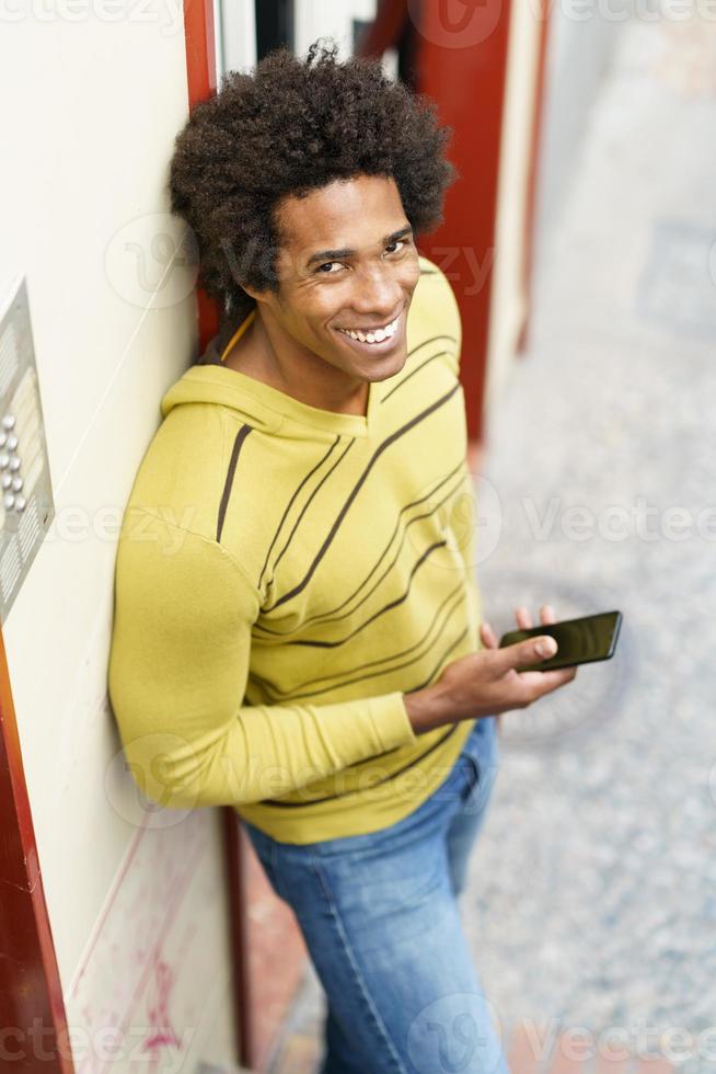 Black man with afro hair and headphones using smartphone. photo