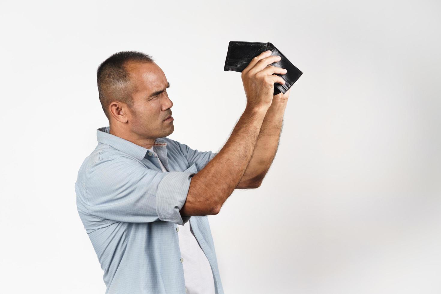 Upset mature man holding and looking inside his empty wallet. photo