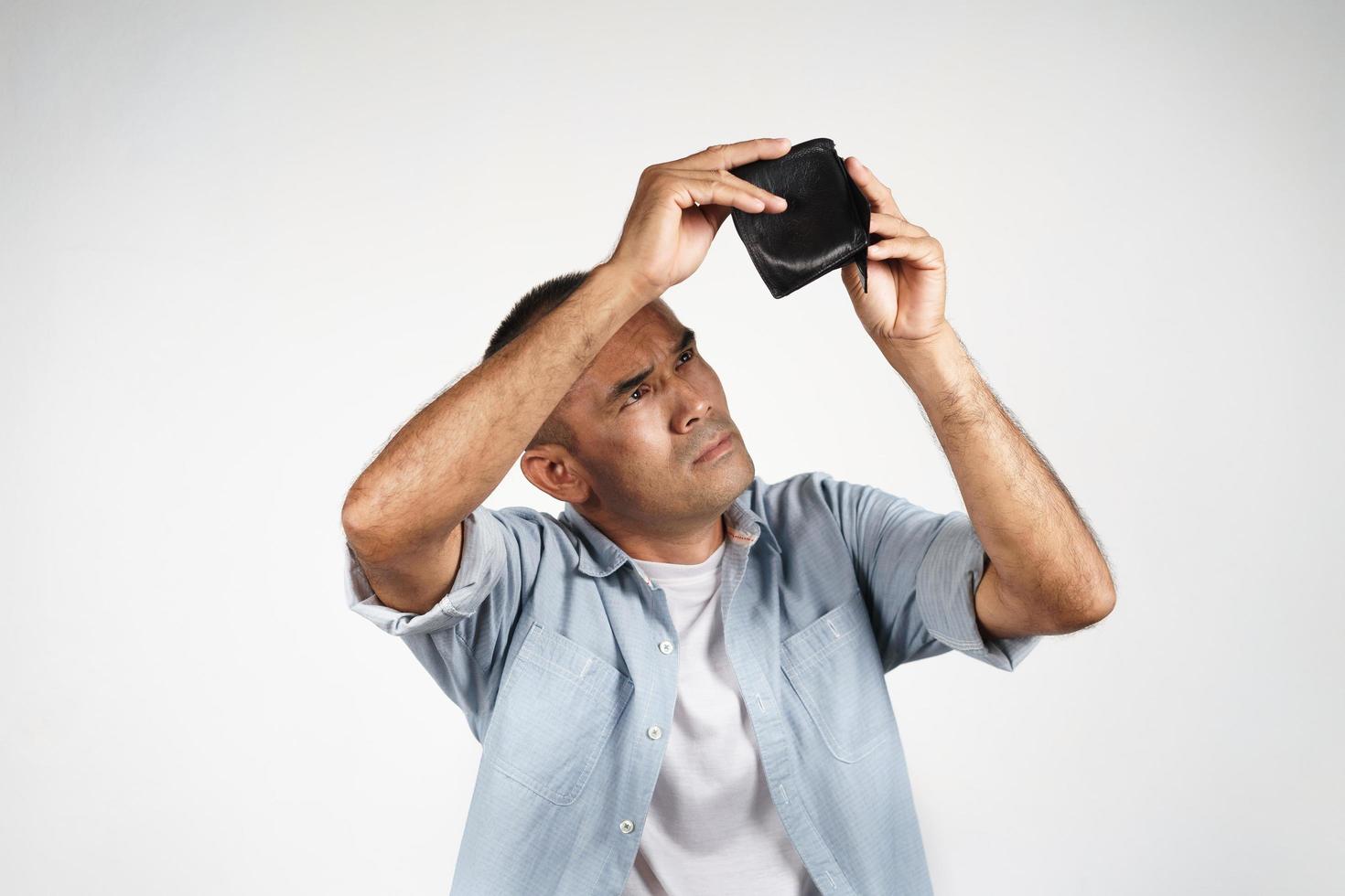 Upset mature man holding and looking inside his empty wallet. photo