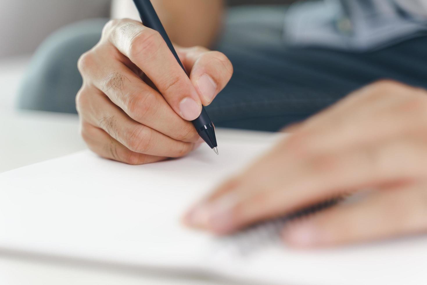 Cerca de las manos del hombre escribiendo en el bloc de notas, cuaderno con lápiz. foto