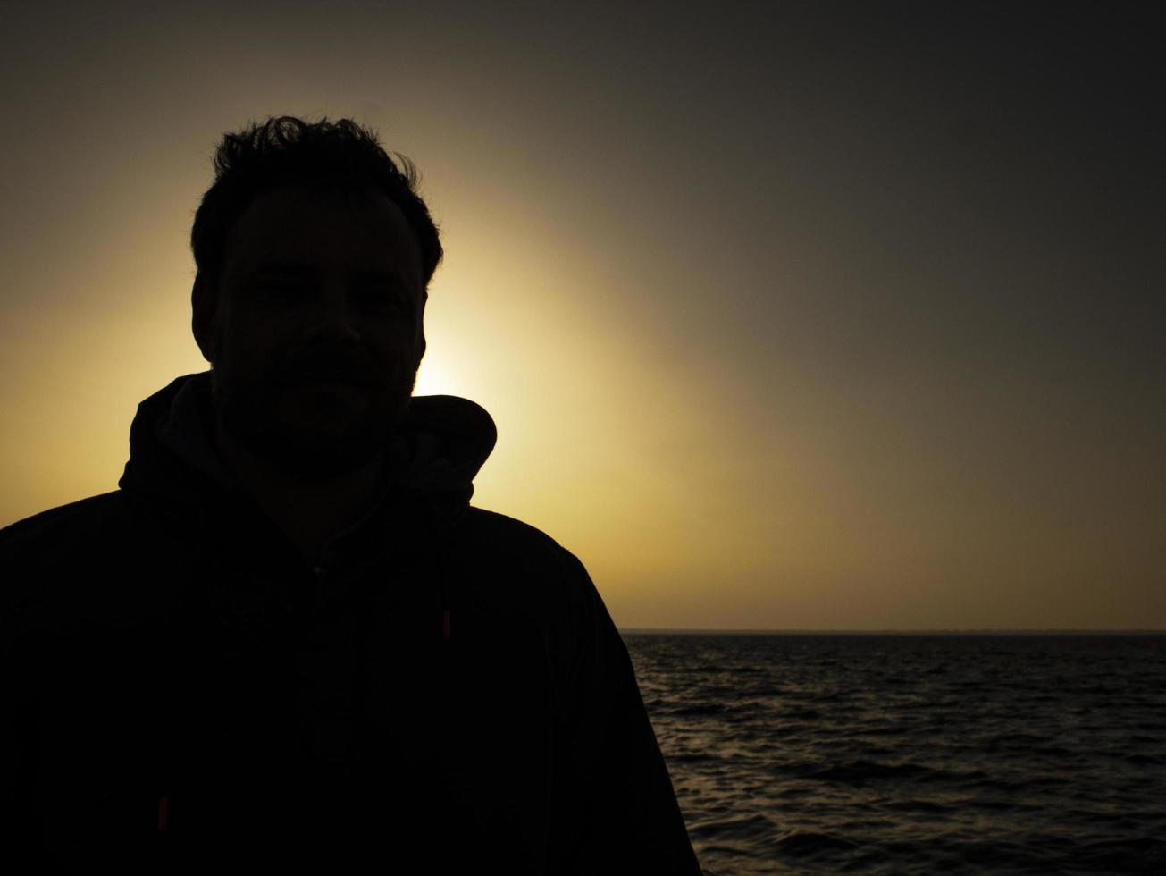 silueta de un hombre de pie contra la puesta de sol cerca del mar foto